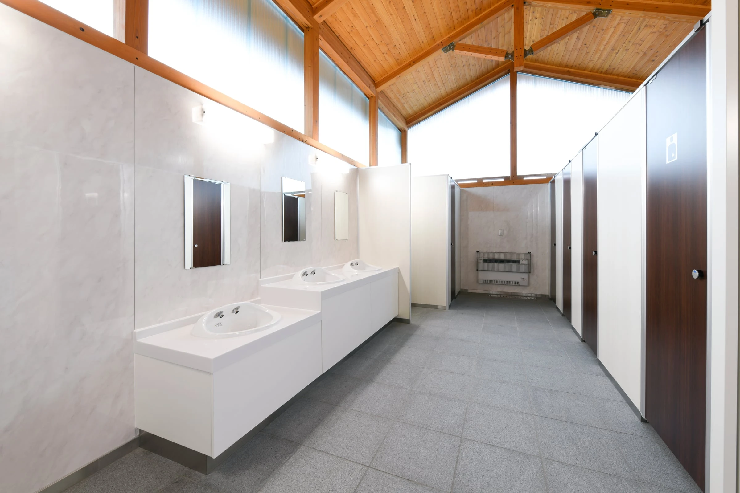 木の小屋組みが見える洗面所。白い洗面台と個室の扉が並ぶ