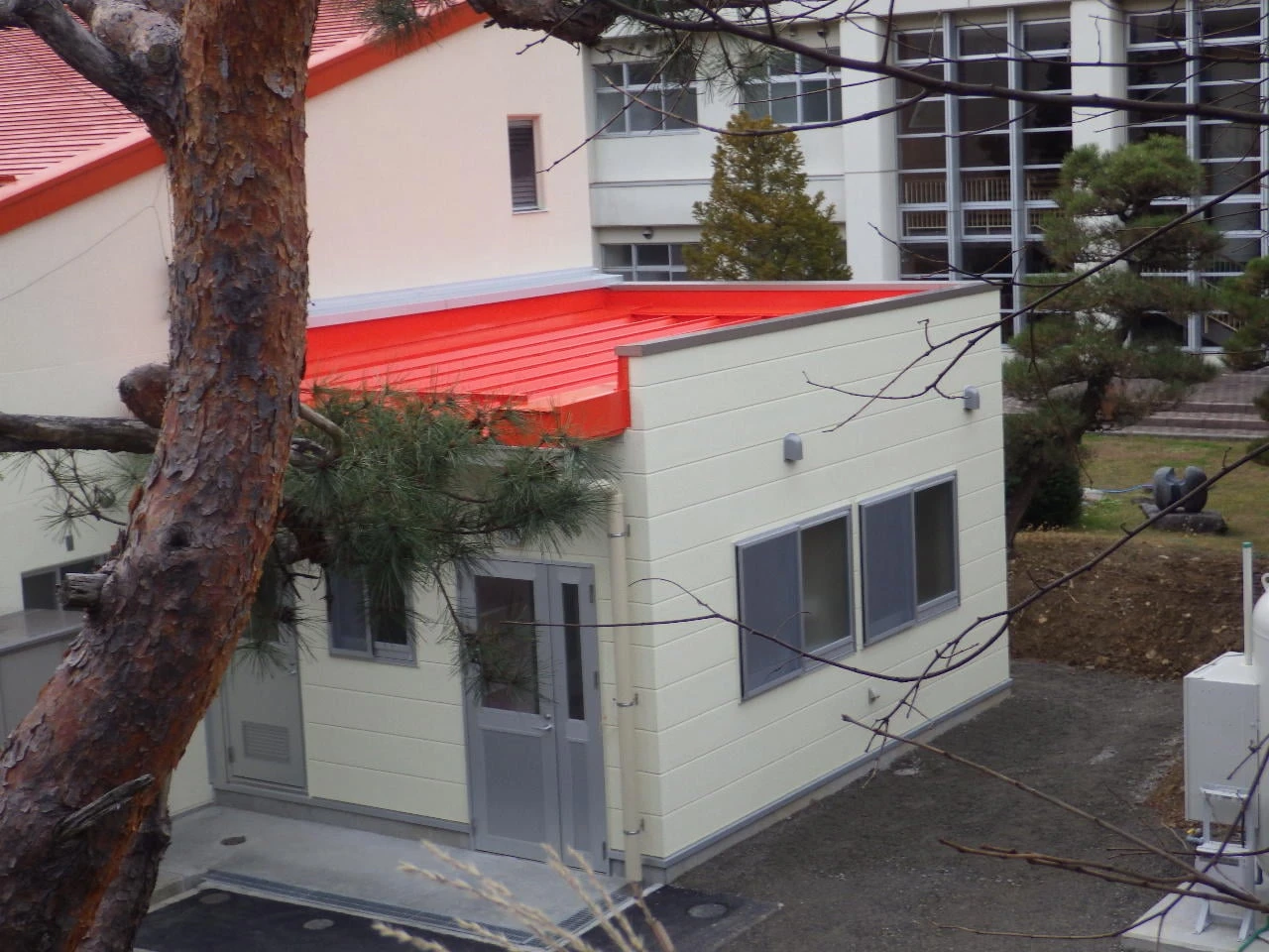 赤い屋根の増築棟と、奥に続く既存の校舎