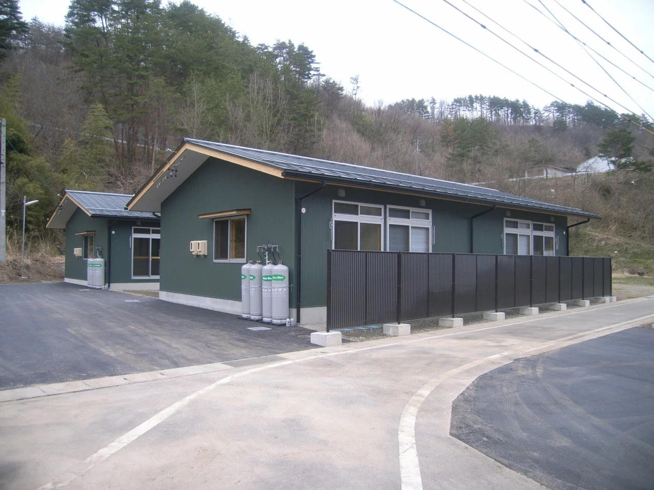 深緑の外壁に改修した平屋の住宅。手前にガスボンベが並ぶ