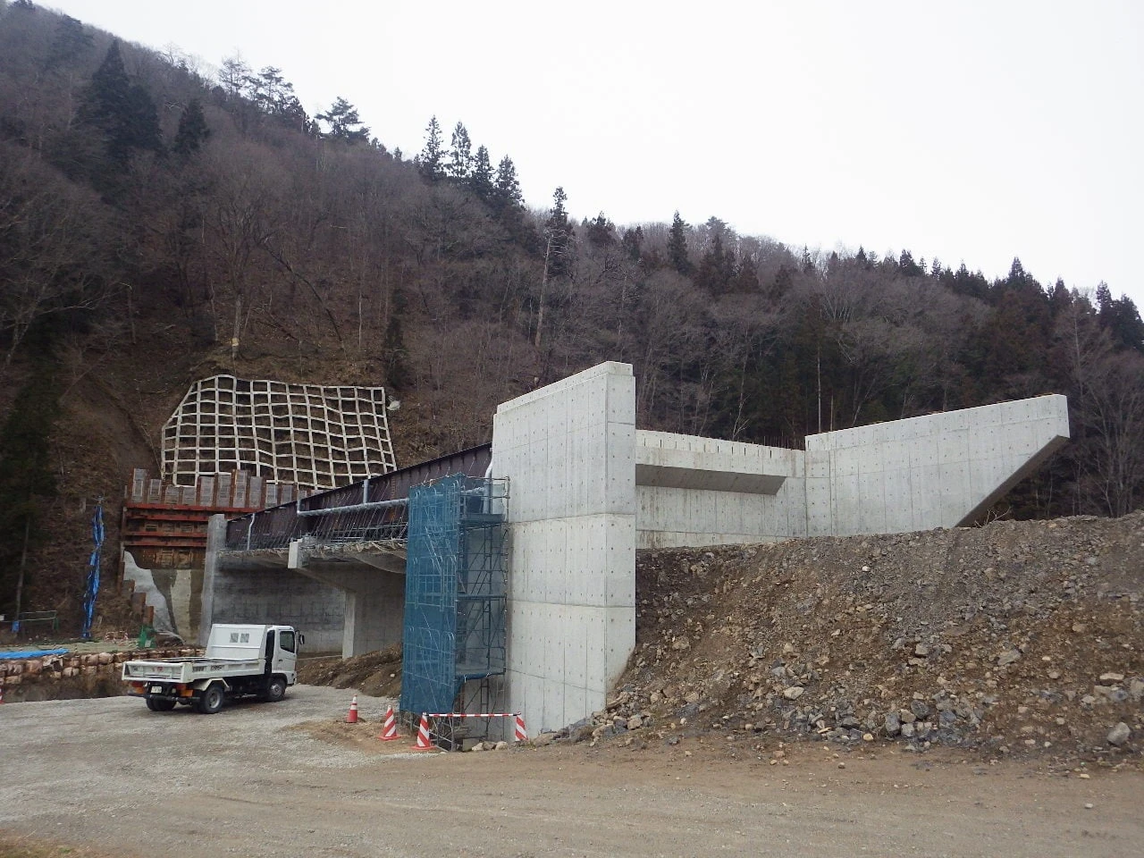 橋台のコンクリートと足場。手前に工事用のトラックが停まる