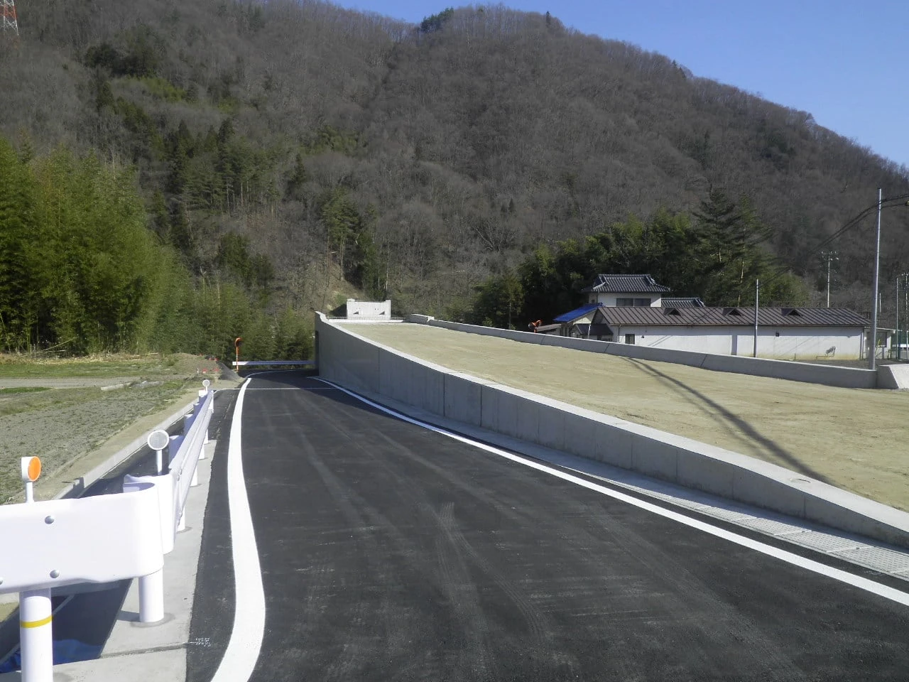 舗装を終えた道路と、右手に続く擁壁と張り芝の法面