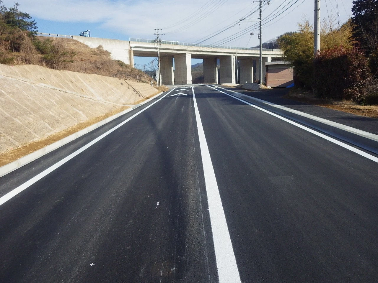 舗装と区画線を終えた道路。奥に高架橋が横切る