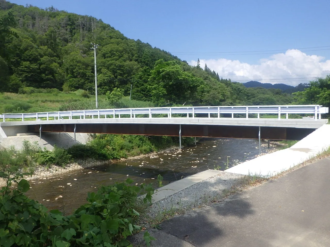 小川に架かる橋を斜めから見たところ。白い高欄と茶色の桁