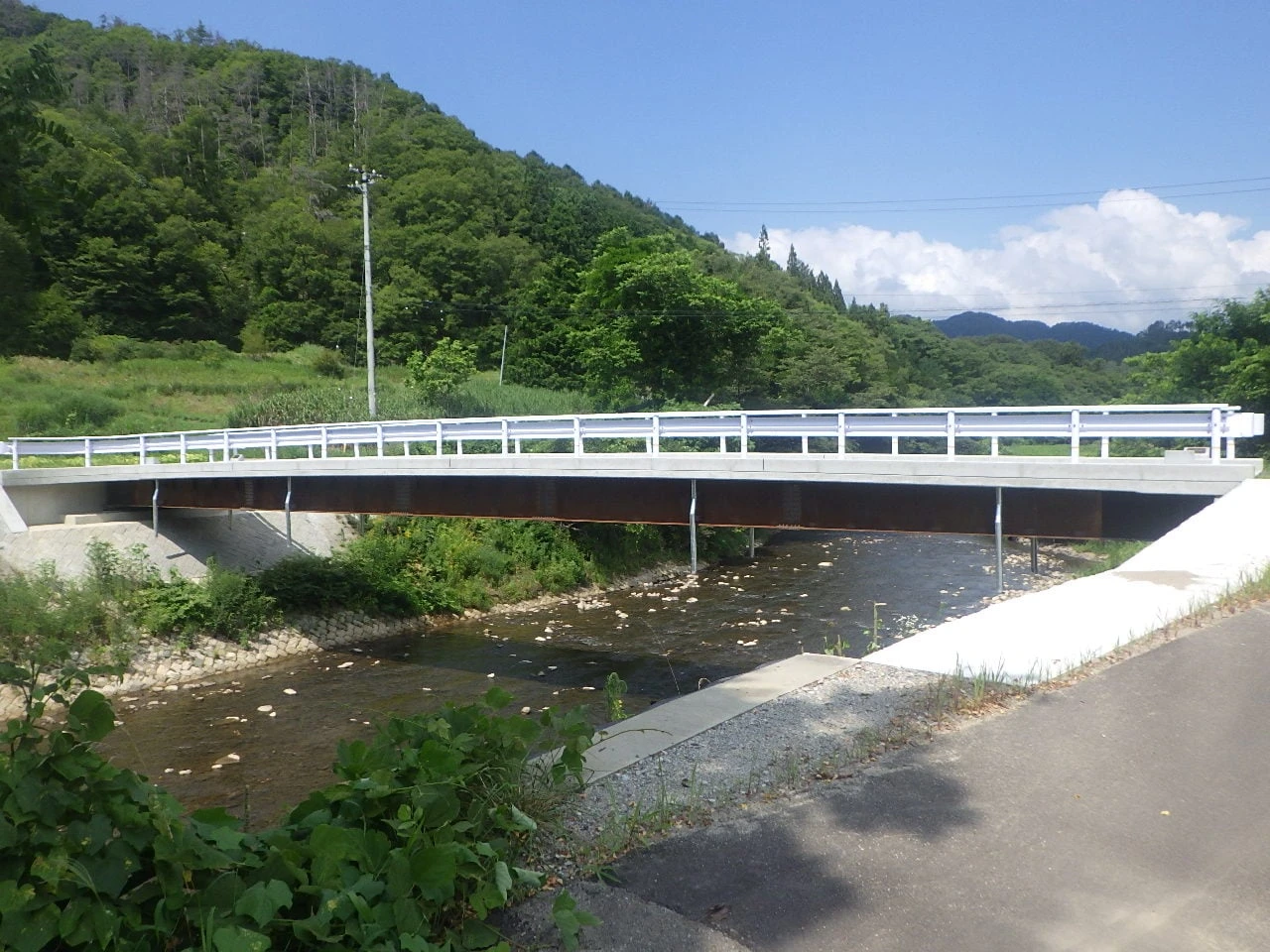 小川に架かる橋を斜めから見たところ。白い高欄と茶色の桁