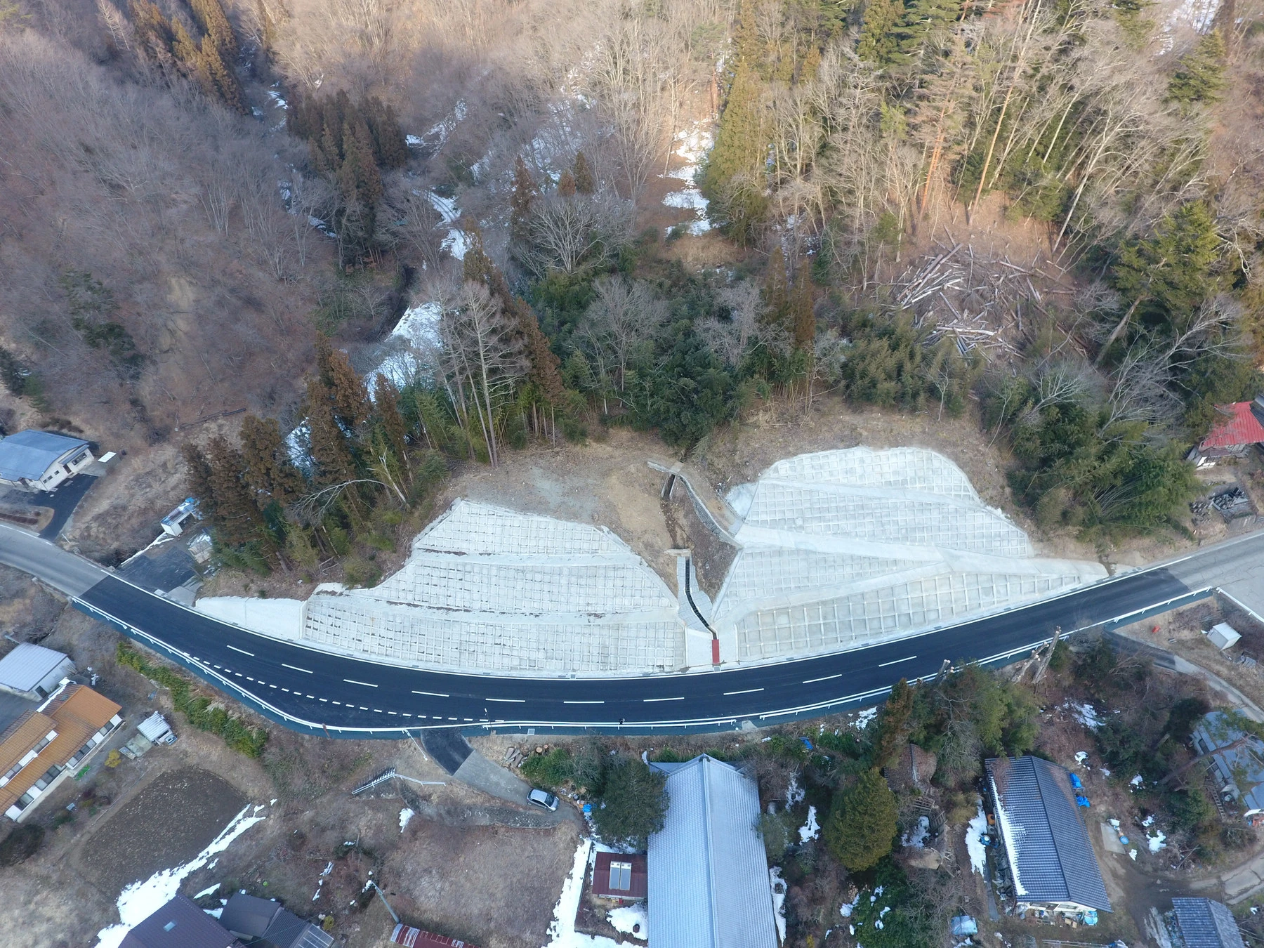 真上から見た、山あいを通る舗装道路と、両側に築いた法枠の斜面