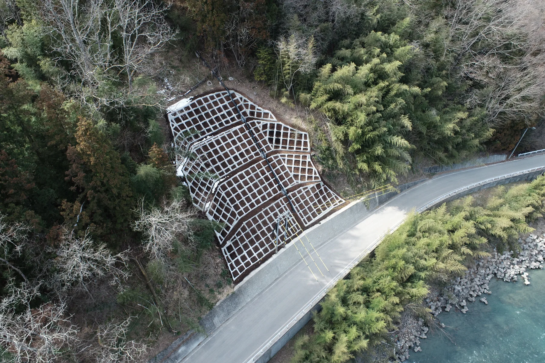 上空から見た、法枠で覆った山の斜面と、その下を回り込む道路と川
