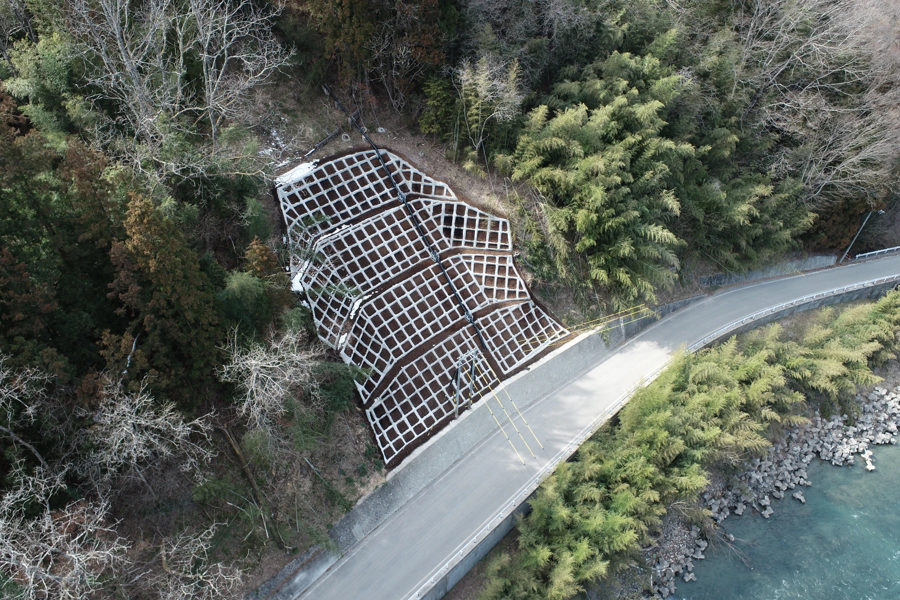 上空から見た、法枠で覆った山の斜面と、その下を回り込む道路と川