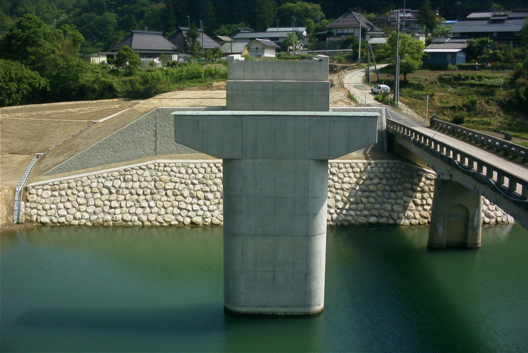 川の中に立ち上がった新しい橋脚と、玉石を積んだ護岸。右奥に既設の橋
