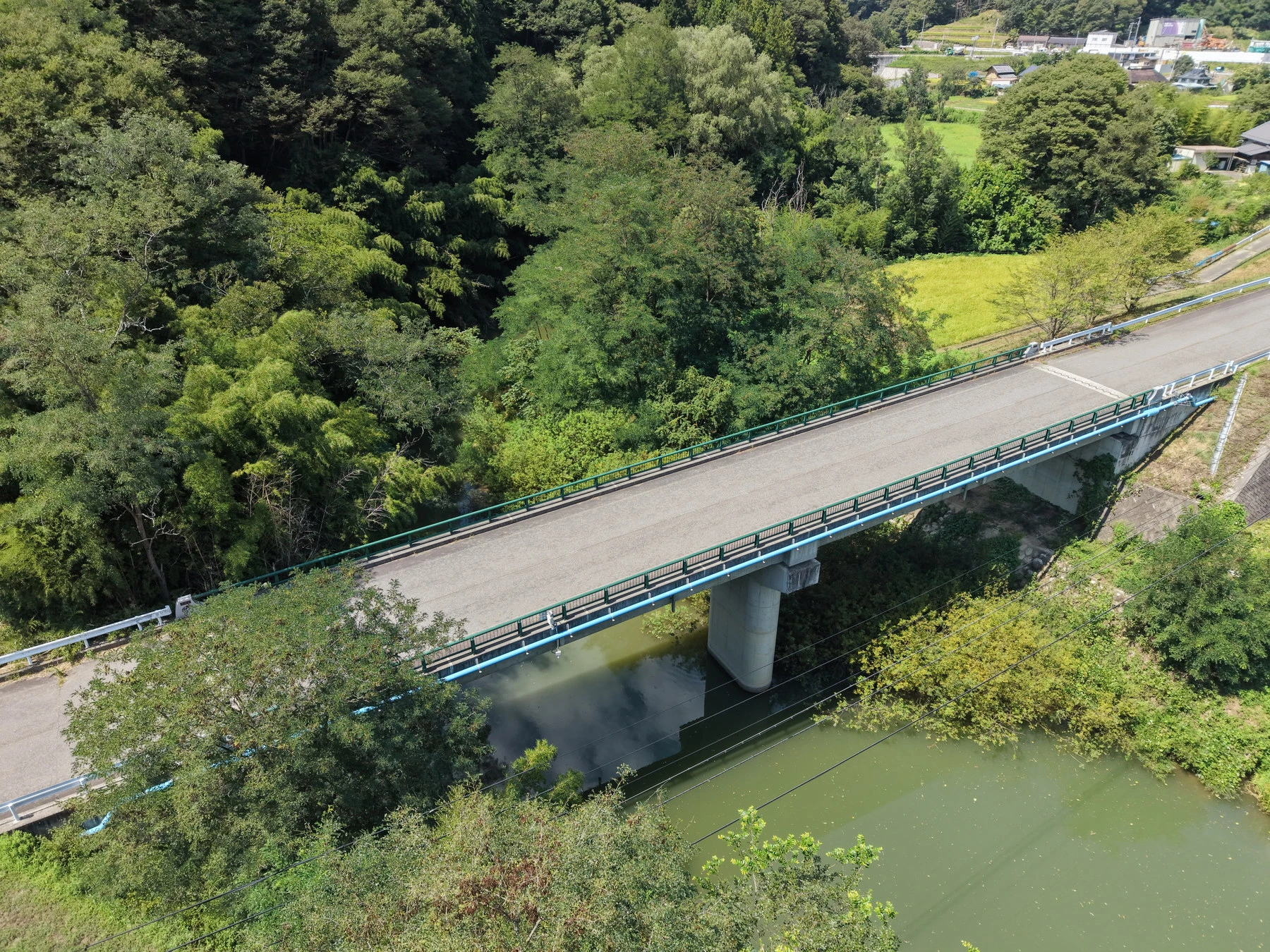 上空から見た、完成した橋の路面と青い高欄。川の中に橋脚が1本立つ