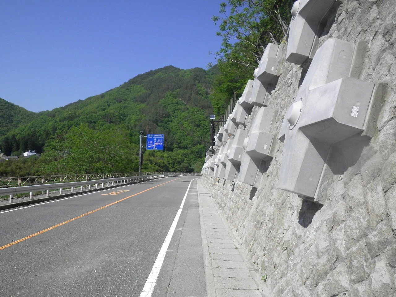 道路から見上げた石積みの擁壁と、そこから突き出した四角い受圧板の列
