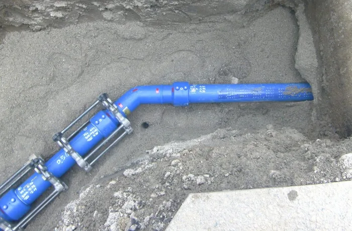 掘削した溝に据えられた青い配水管と、継手を締める金具