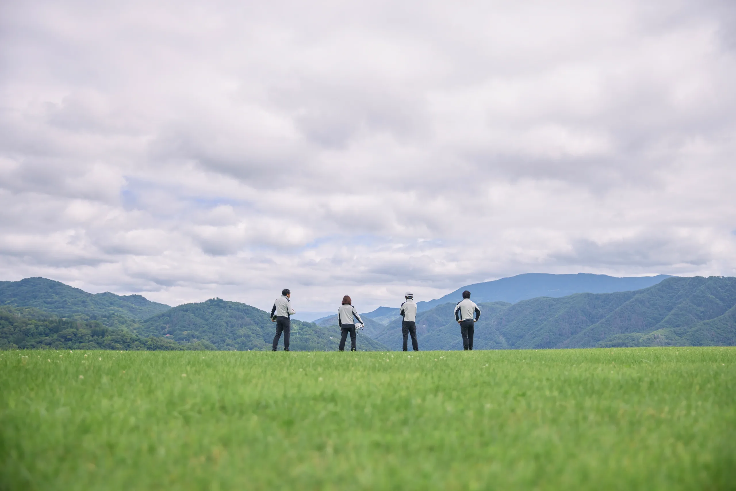 生坂村を見下ろす丘に並んで立つ4人の社員