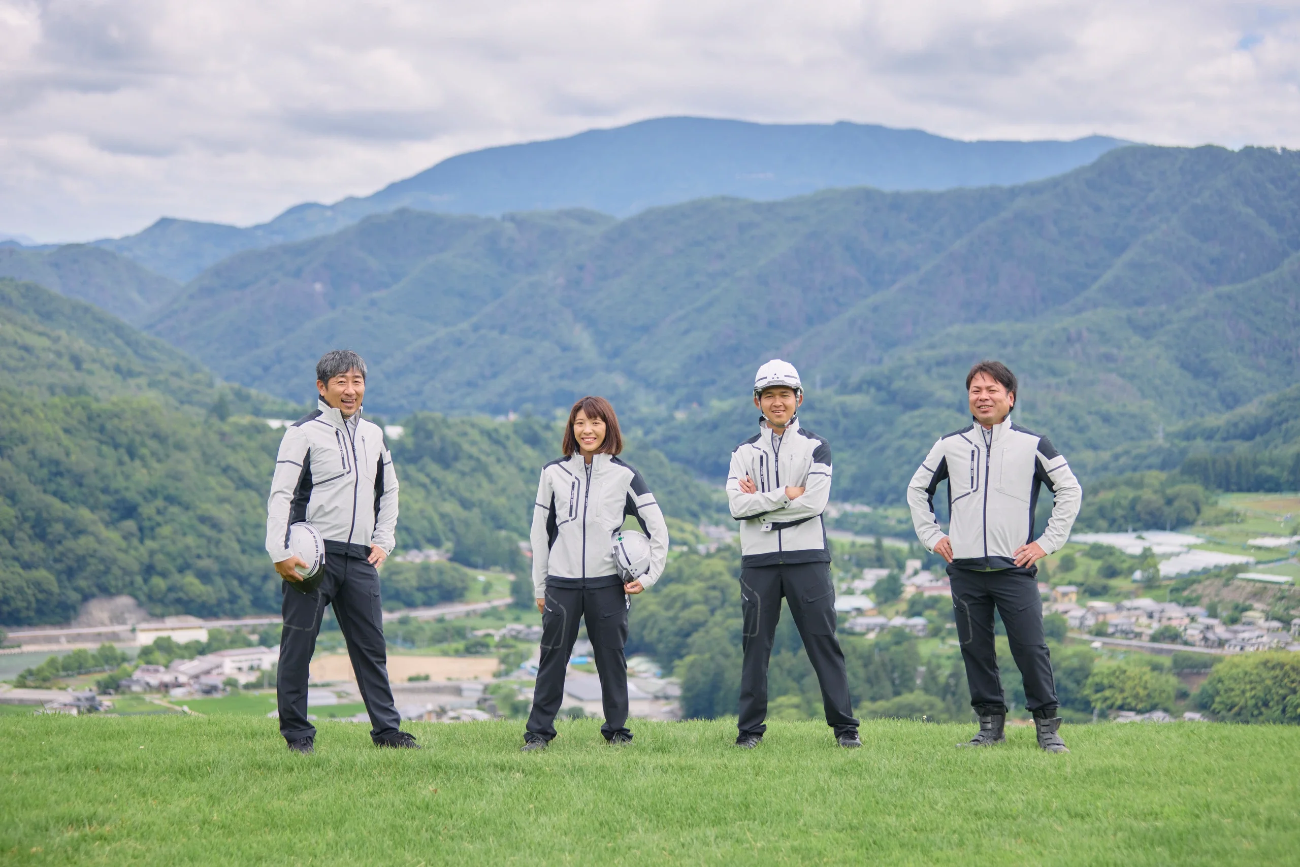 丘の上に並んで立つ4人の社員と生坂村の山並み