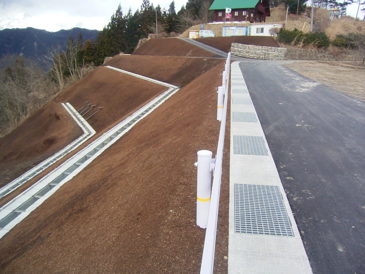 完成後、道路の上から見た法面と排水路。奥に山小屋風の建物