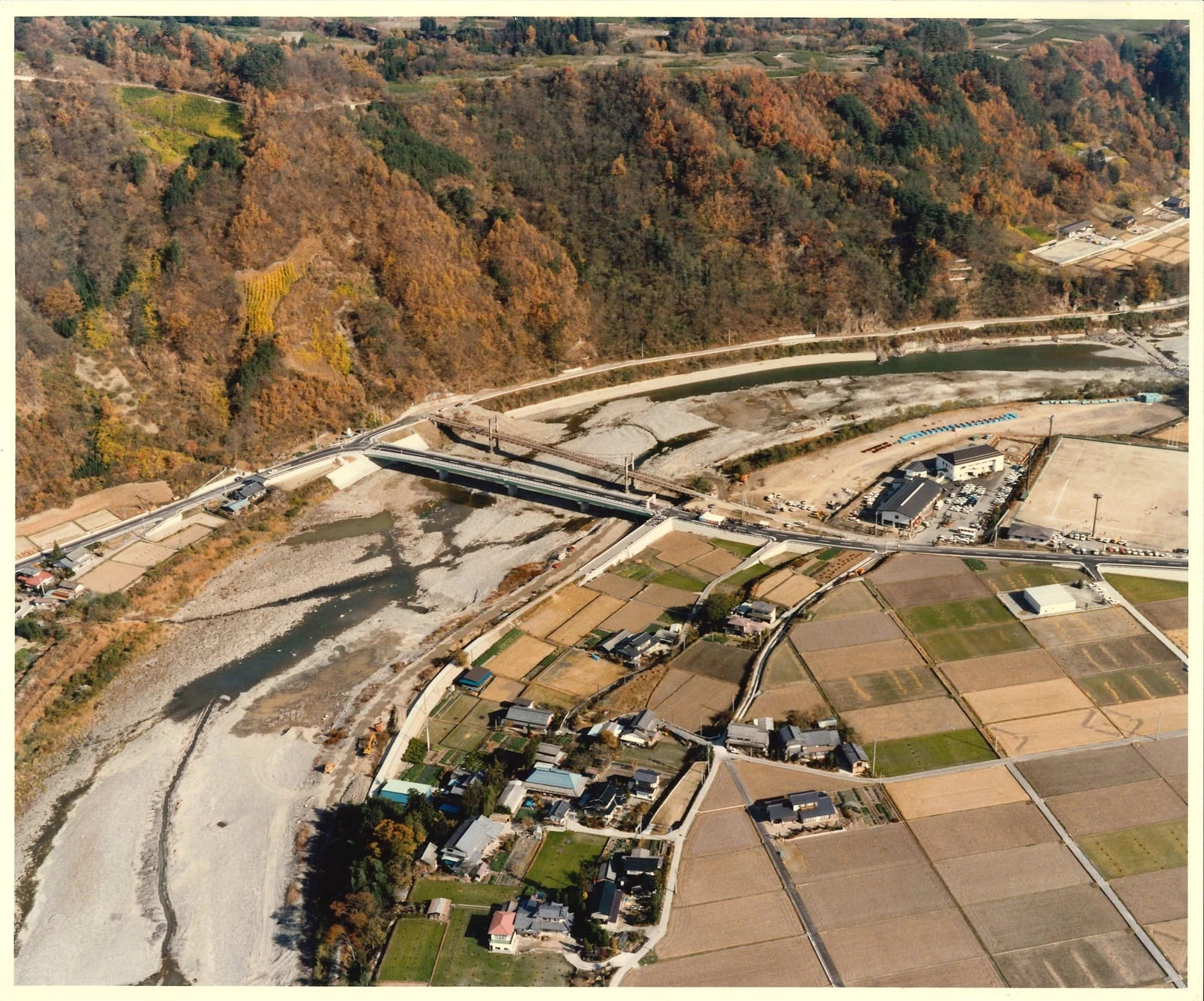 当時の空撮写真。川をまたぐ橋と、河原に設けられた工事ヤード、周囲の集落と田畑