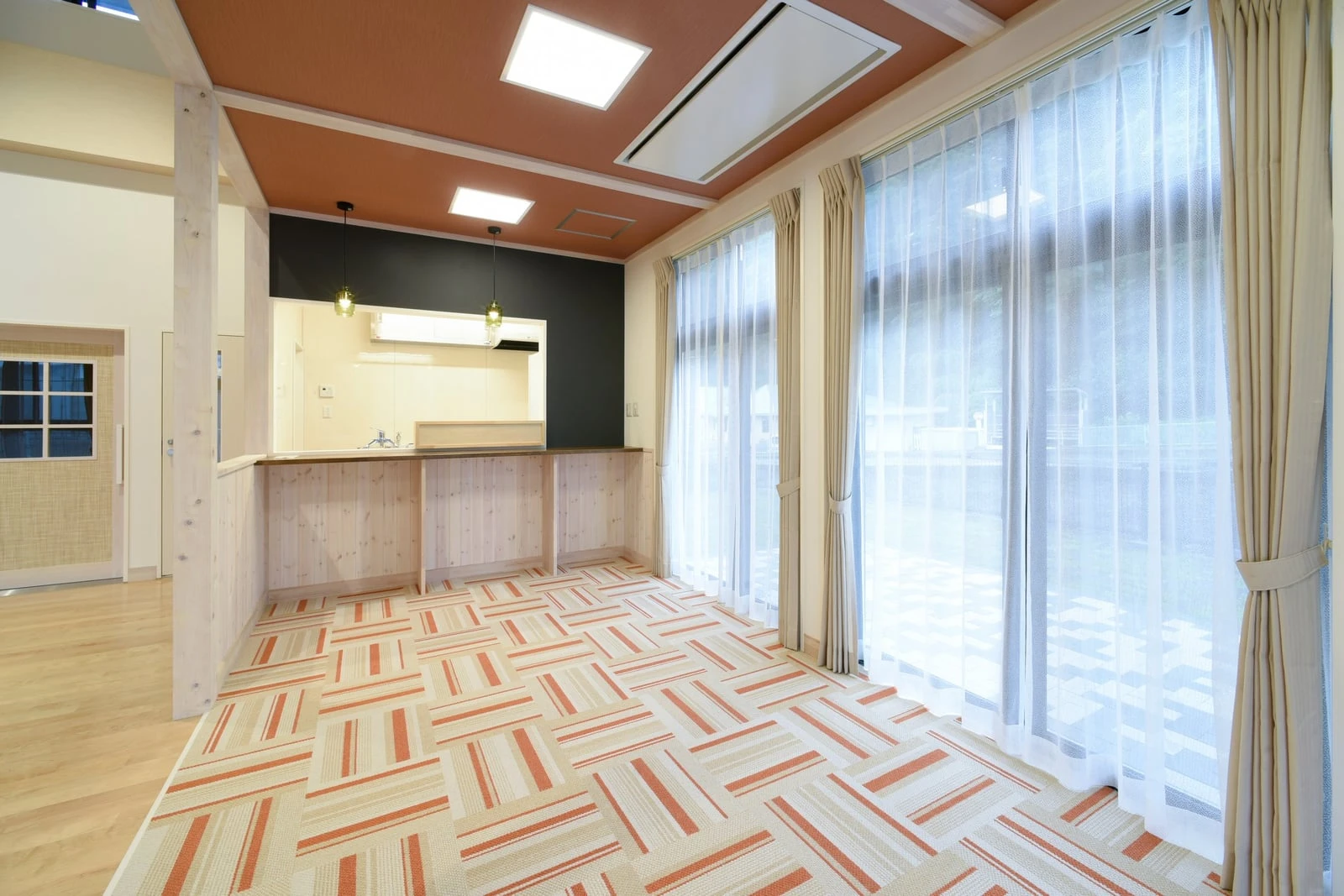 オレンジ色の天井と木のカウンターがある部屋。窓際に市松模様の床が広がる