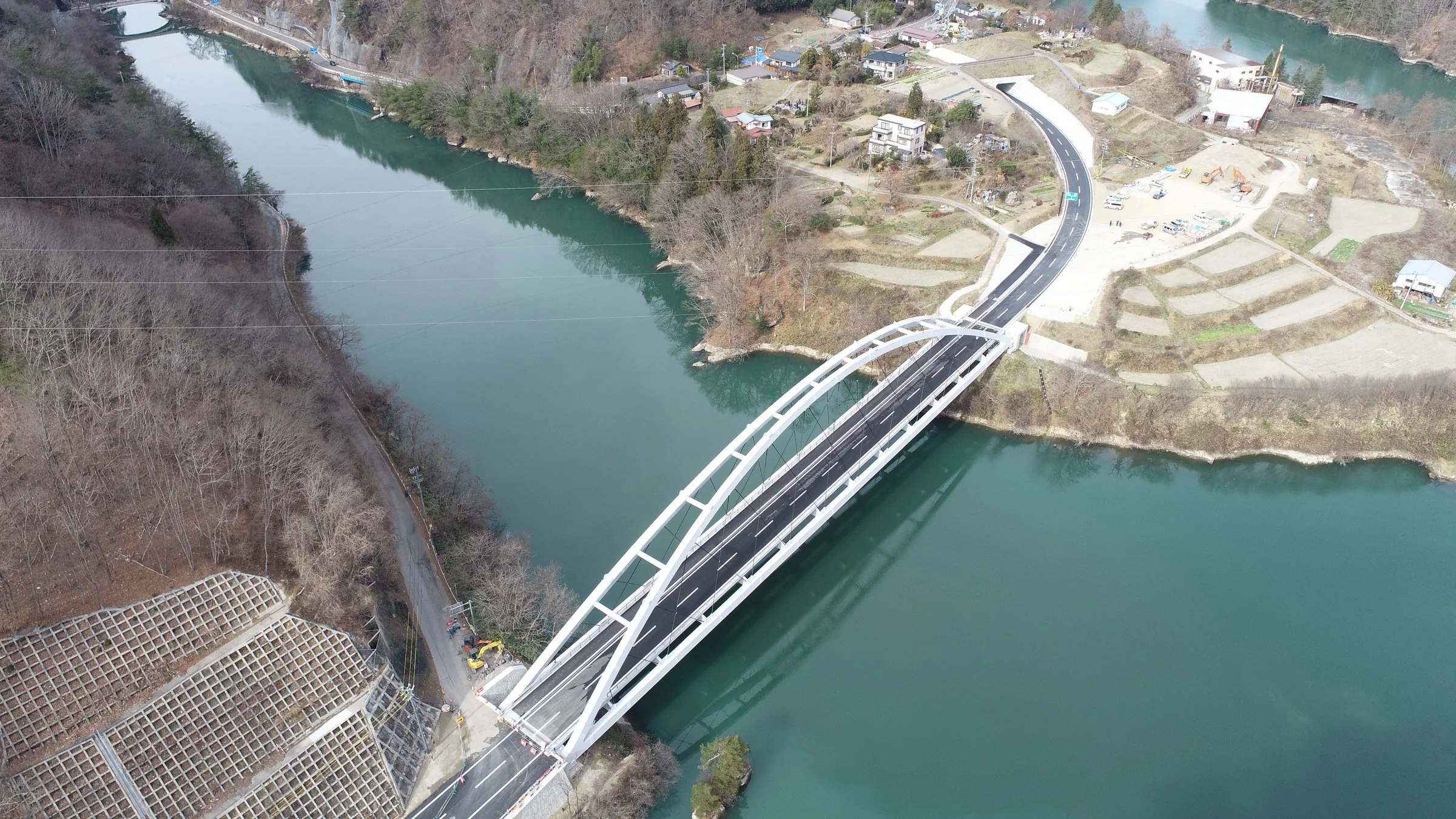 上空から見た、川に架かる白いアーチ橋と、対岸へ続く道路