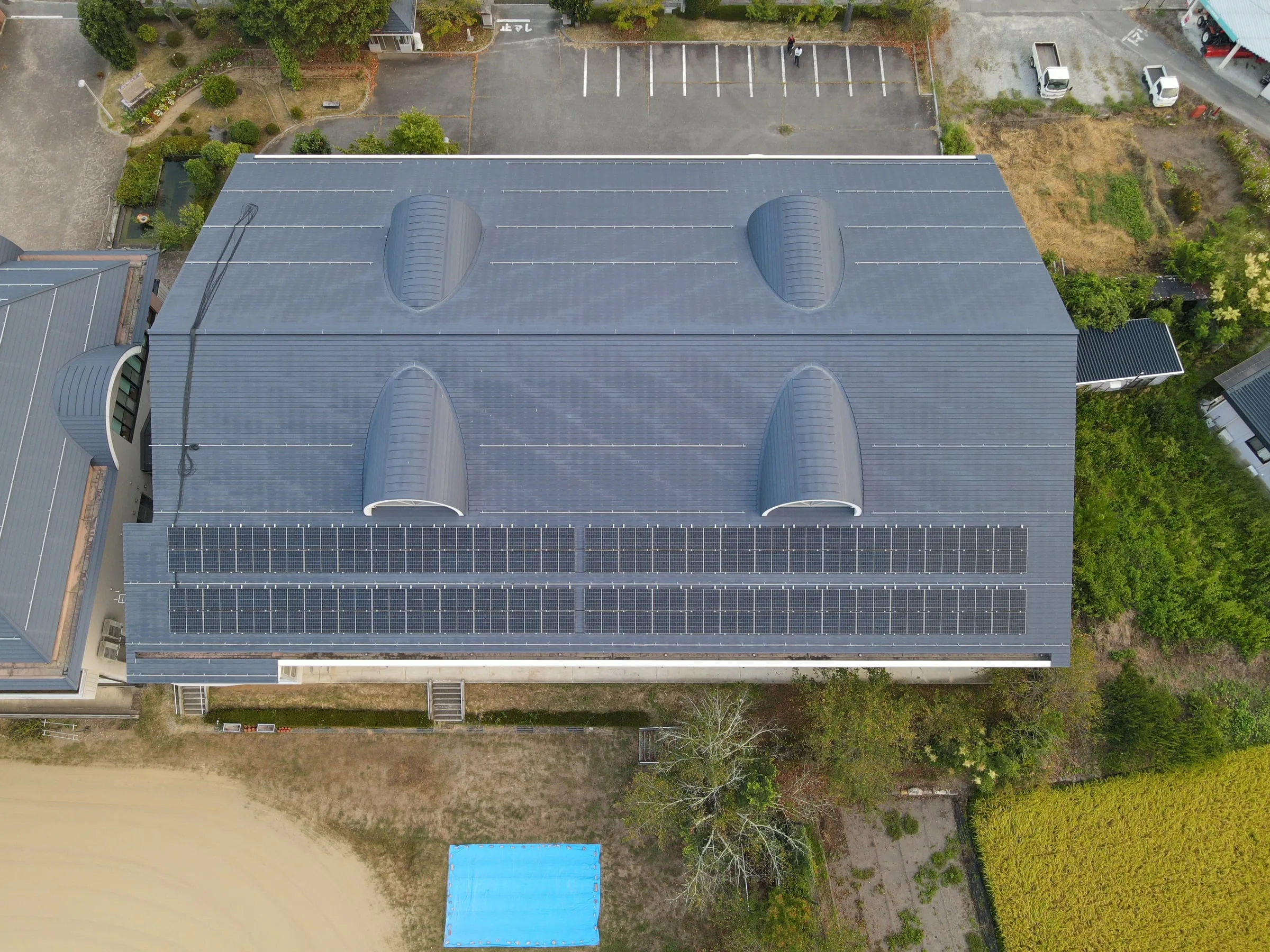 体育館の大屋根の斜面に並ぶ太陽光パネルを上空から見た様子