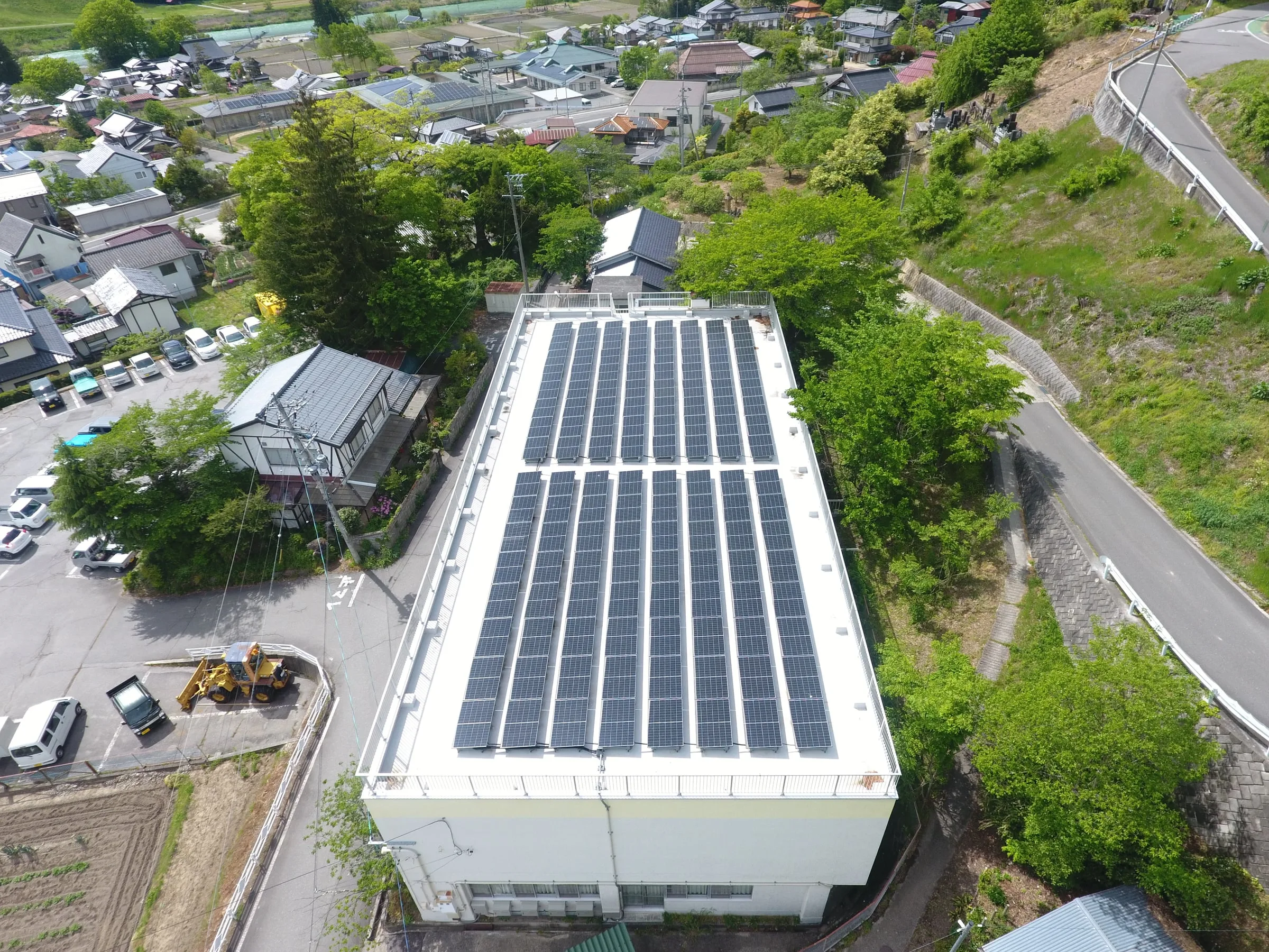 白い建物の陸屋根いっぱいに、架台で並べた太陽光パネル