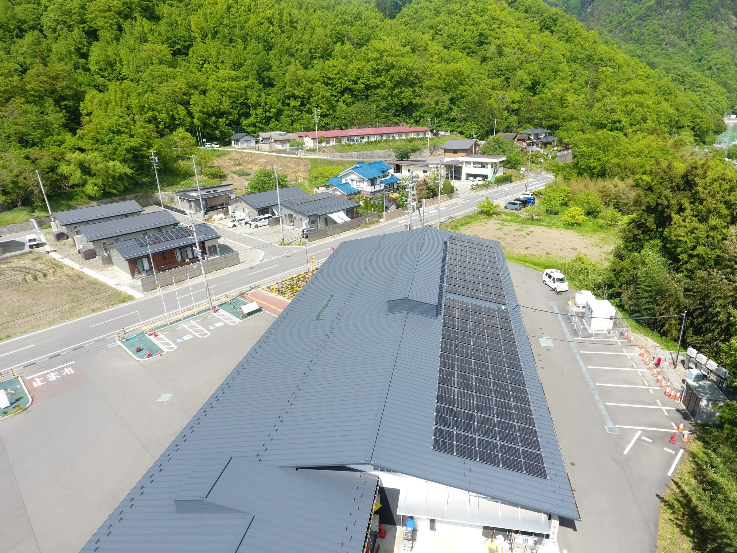 道路沿いの施設の大屋根に設けた太陽光パネルと、背後の山